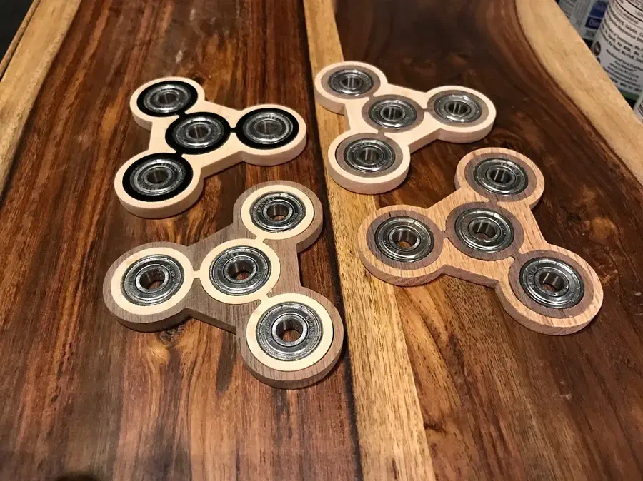 Four wooden spinners with contrasting wood inlays and installed bearings on a striped wooden surface