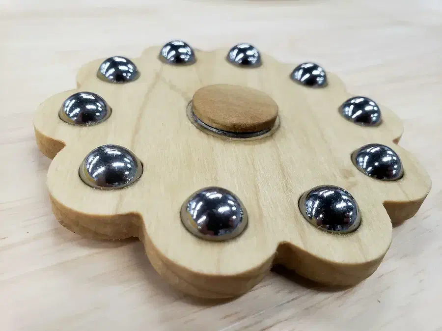 A flower-shaped pale wooden spinner with steel balls around the edge and a wooden center cap