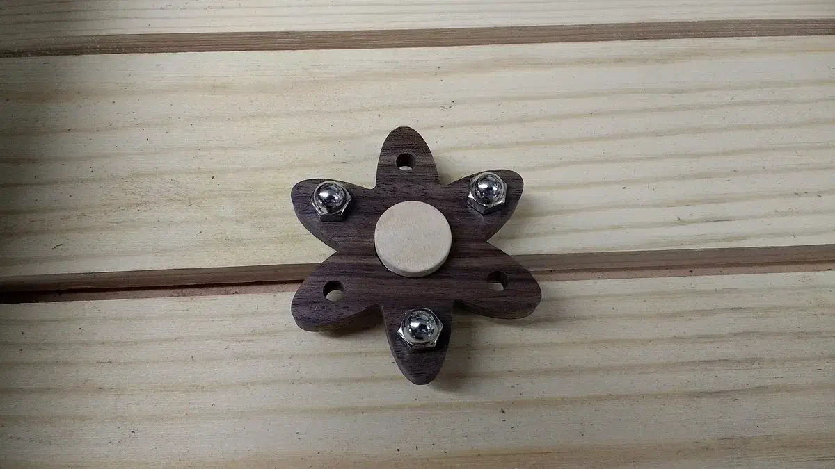 A small wooden character-shaped spinner with a center finger pad and metal end weights
