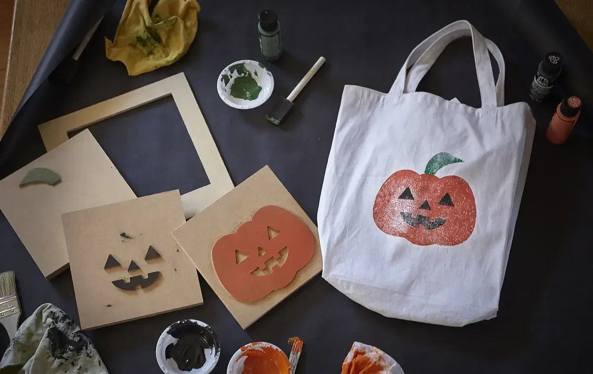 Three carved MDF printing blocks and a square positioning guide beside a white bag printed with an orange, green and black pumpkin