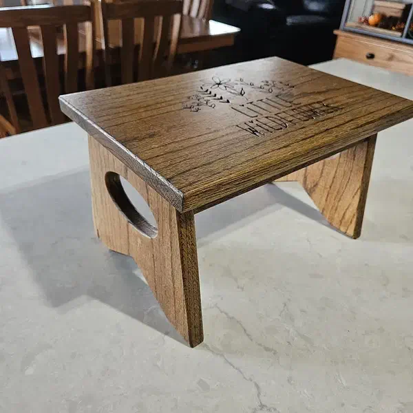 A stained wooden step stool with carved lettering on the top and oval openings in the side legs