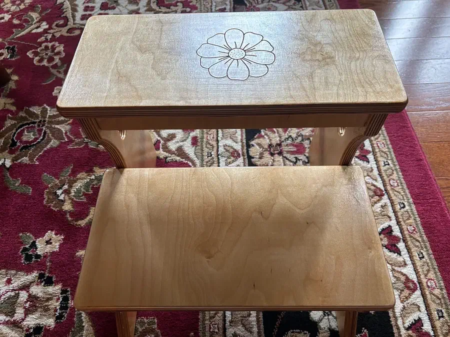 A pale plywood two-step stool with a carved shamrock on the upper tread