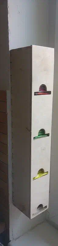 A complete tall birch-plywood tea dispenser beside a window, with four openings showing different tea packets.