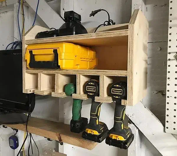 A finished plywood drill-storage cabinet holding three cordless drills and chargers