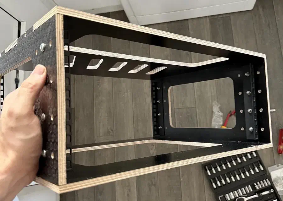 An assembled plywood fly-rack sleeve with separate black metal rack rails installed inside