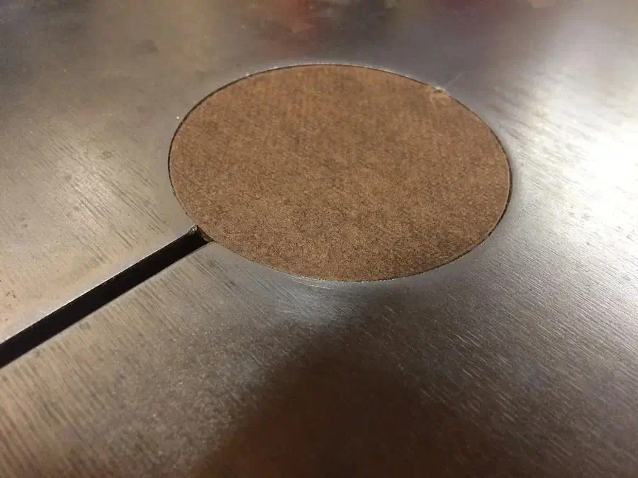 A circular hardboard insert sitting in a metal bandsaw table opening