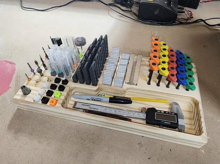 Pine tool board holding colored router bits, clamps, pencils and a digital caliper