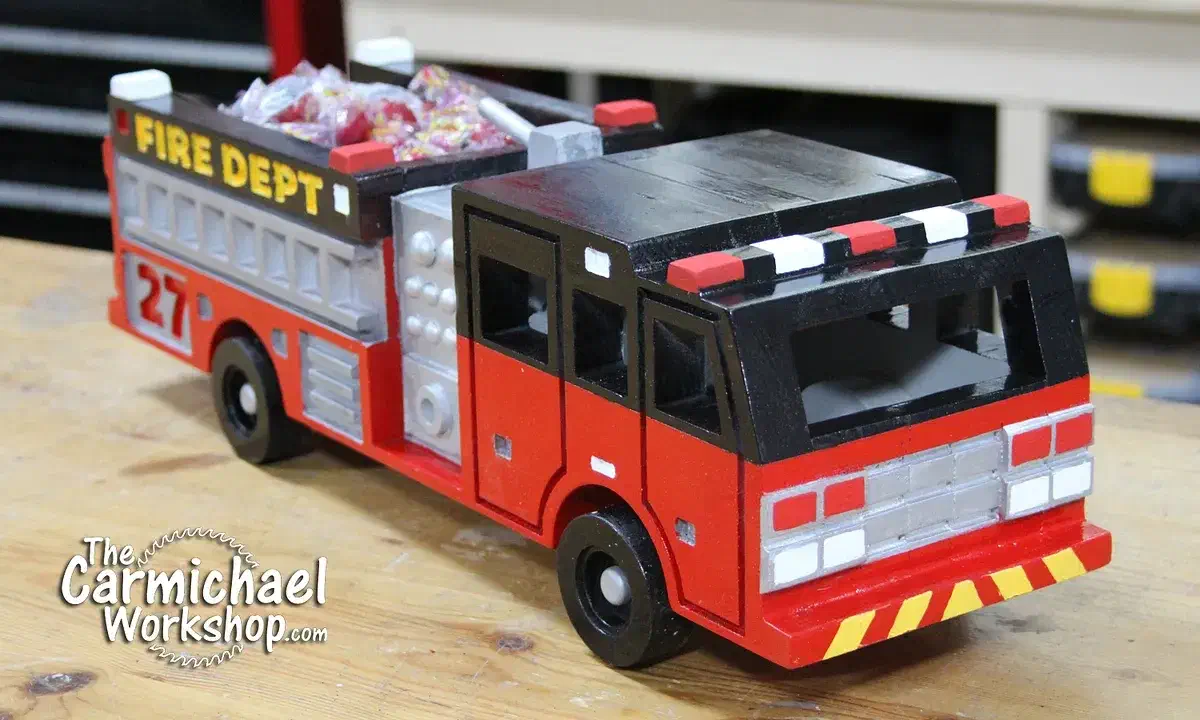 A red, black and silver wooden fire engine with an open rear bed holding wrapped candy