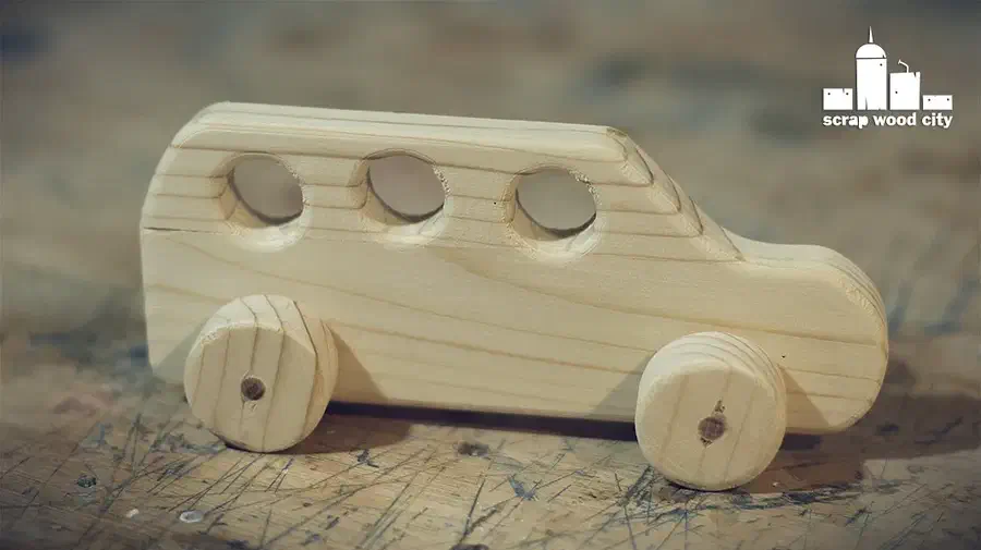 A pale wooden toy car with three round windows and wooden disc wheels on a workbench