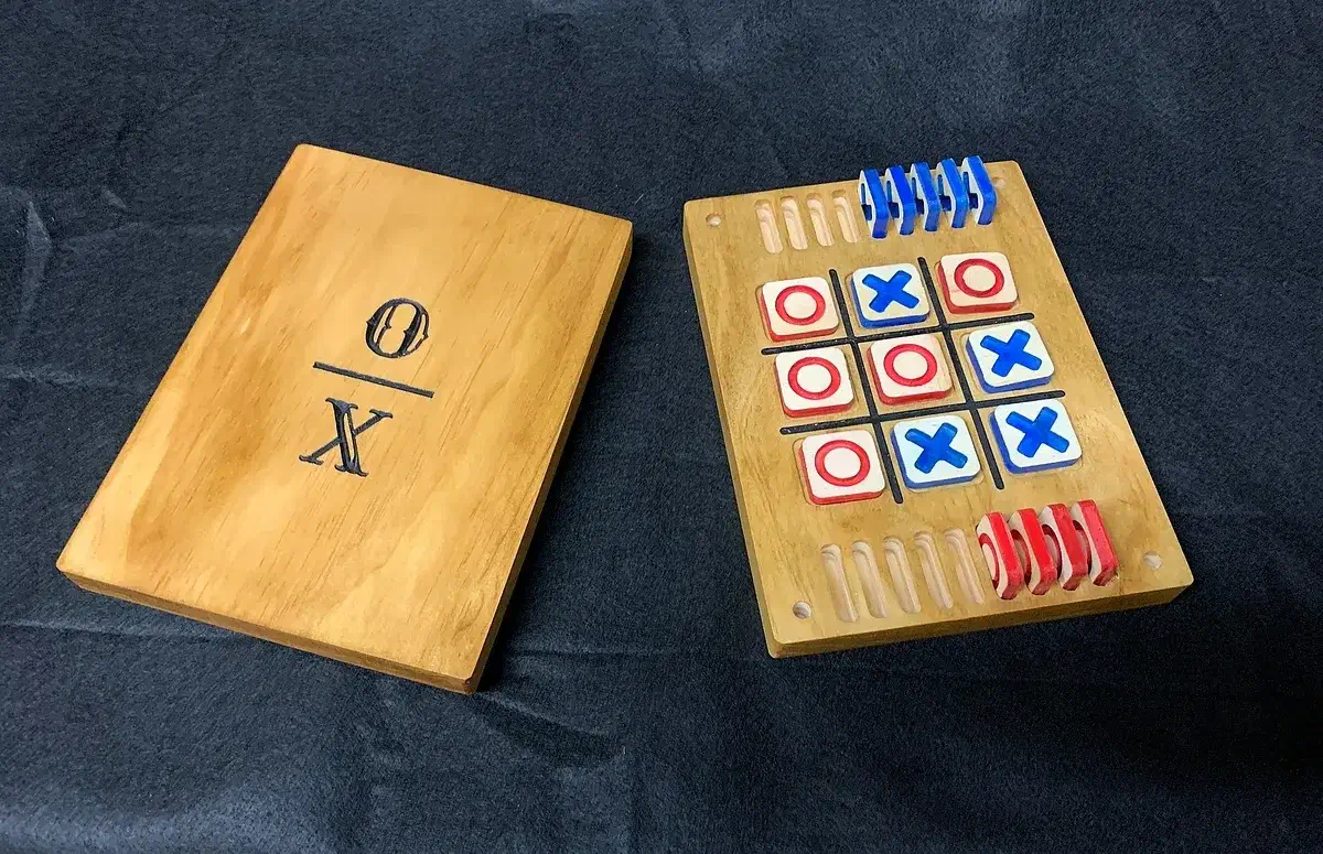 A painted wooden tic-tac-toe board with red and blue pieces and a separate wooden lid marked X and O
