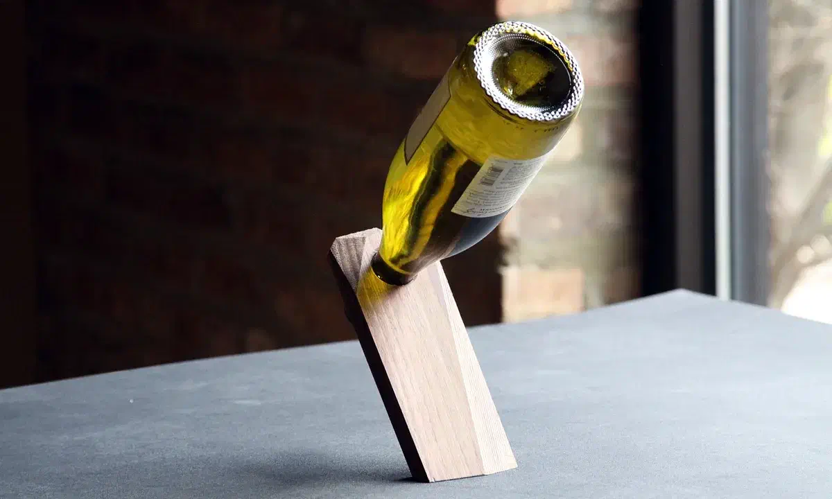 A pale faceted wooden holder balancing a green wine bottle on a table