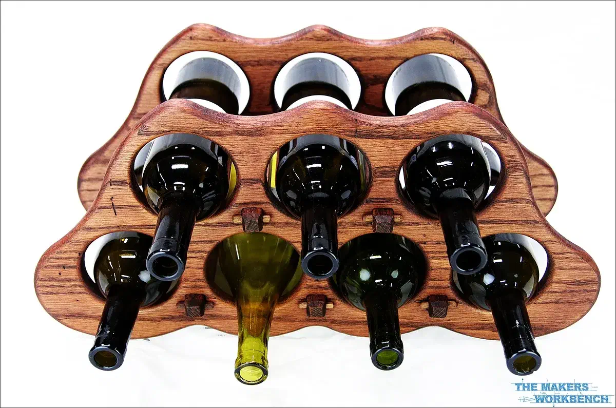A finished curved wooden wine rack holding bottles, with The Makers Workbench source mark at the lower right