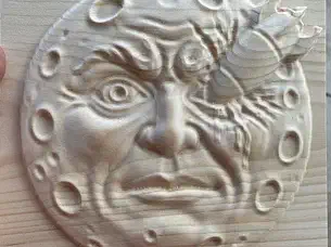 A detailed moon face bas relief carved into a square wood panel
